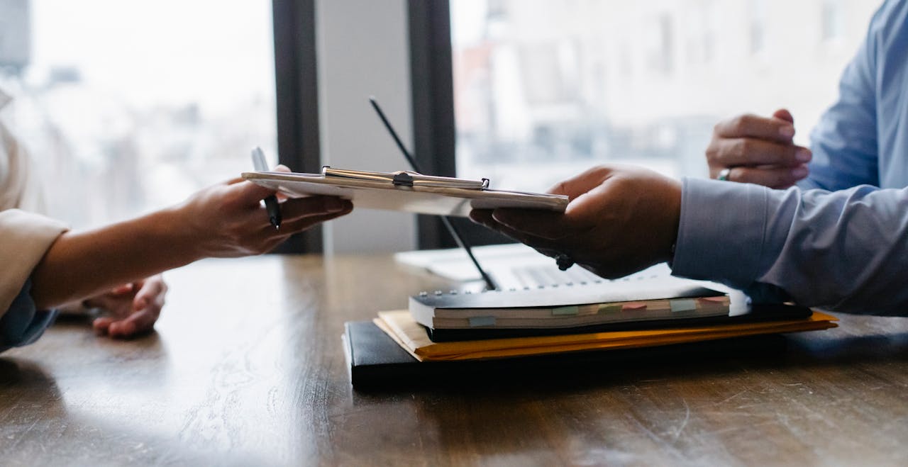 Home Crop anonymous ethnic woman passing clipboard to office worker with laptop during job interview